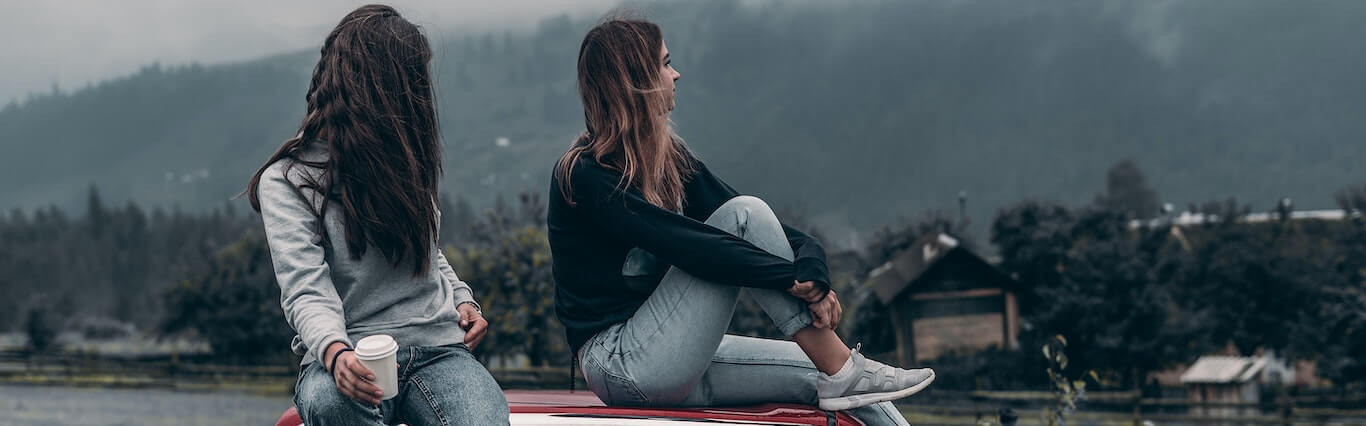 Two teens sitting on a car